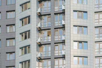 Fototapeta premium Modern residential building, symmetrical facade with gray and white windows, balconies, gray railings, natural lighting from left, angled upward perspective