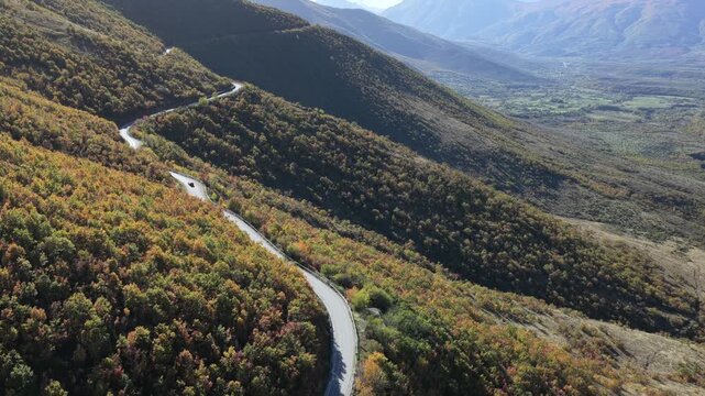 A winding mountain road near Demilaj surrounded by dense autumn forests and views toward the Bajram Curri valley.
