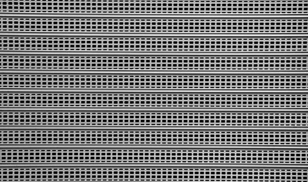 Gray steel Roller Shutter Door Background with sunlight shadow on surface corrugated Grey metal mesh curtain door entrance to store Perforated gray silver iron Garage Security door background backdrop