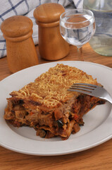 Part de lasagnes aux l&eacute;gumes maison servie dans une assiette avec une fourchette en gros plan servie &agrave; table avec un verre d'eau