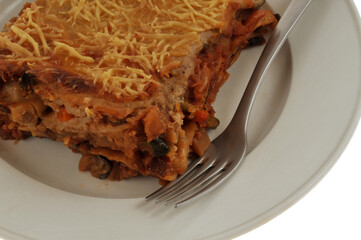 Part de lasagnes aux l&eacute;gumes maison servie dans une assiette avec une fourchette en gros plan