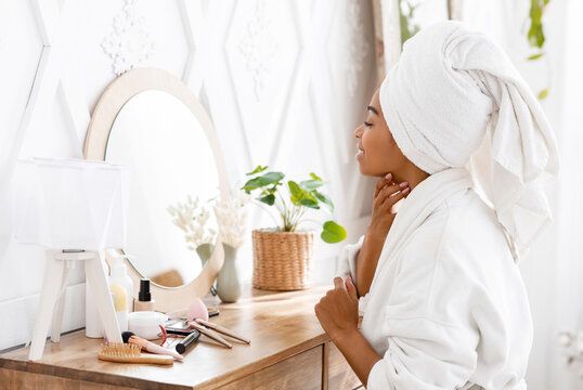 Pampering Day Concept. Attractive African Woman Wrapped in Bathrobe And Towel Sitting At Dressing Table, Ready For Beauty Treatments At Home