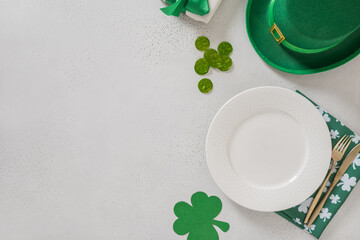 St Patricks Day banner with white plate, cutlery, table setting, gift, leprechaun hat and clover leaves on white background. View from above. Copy space.