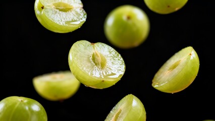Fresh green gooseberries falling, with some cut in half showcasing their juicy interior against a dark background