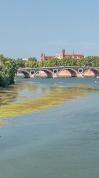 Garonne River and Pont Neuf timelapse in downtown Toulouse, France. Renaissance arch bridge reflects in the water under a blue sky with Basilica of Our Lady of the Daurade. Waterfront with green trees