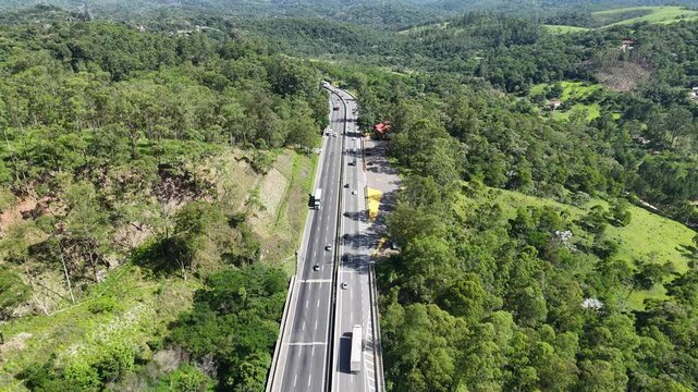Rodovia com tr&aacute;fego intenso de ve&iacute;culos atravessando &aacute;reas urbanas e verdes, representando log&iacute;stica, mobilidade e integra&ccedil;&atilde;o entre regi&otilde;es.