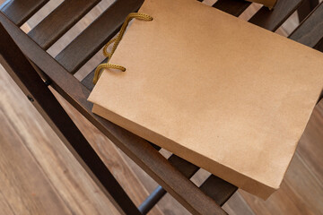 Kraft paper bag. Brown paper shopping bag mockup with rope handle on wooden chair. Retail packaging design template for boutique, gift or sale promotion. purchase, gift, sale
