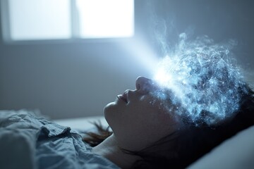 Woman lies on bed with digital projection of thoughts glowing from her head in a simple room