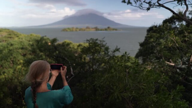 A mature woman hikes through Charco Verde park, enjoying views of the volcano and taking pictures on Ometepe Island in Nicaragua.