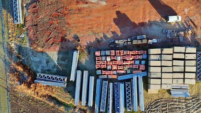Aerial view of construction site with excavator stacked building materials and service vehicles captured by drone