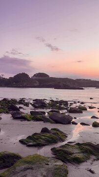 Panoramic view of a sandy and rocky beach at sunset with gentle waves breaking on the sand as the sun sets on the horizon, Porcia Beach, El Franco, Asturias, Spain 