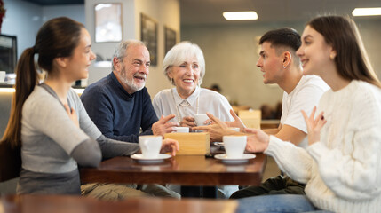 Lively conversation between family generations. Young couple restaurants customer with senior colleagues are sitting at table, talking, laughing, joking, chatting, and spending time with friends. .