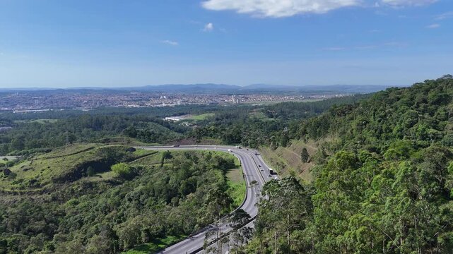 Vis&atilde;o a&eacute;rea de rodovia na serra de Mogi das Cruzes cortando &aacute;rea verde preservada, destacando integra&ccedil;&atilde;o entre infraestrutura vi&aacute;ria, relevo montanhoso e mobilidade regional no Alto Tiet&ecirc;.