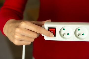 close-up of a woman pressing a red button on the power strip. She's wearing a red sweater. A symbol of high prices and energy poverty.