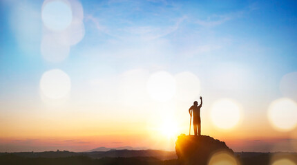 Silhouette of businessman standing on top of mountain and raised his hand up to success.