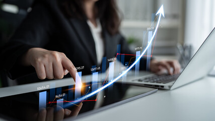A focused businesswoman uses a laptop to analyze financial data, represented by digital graphs showcasing growth and success in a modern office setting. Scalp