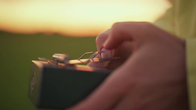 hands adjust light meter at sunset in meadow, photographer calibrates analog exposure meter with careful fingers, warm golden glow, shallow depth of field, tactile closeup of vintage device
