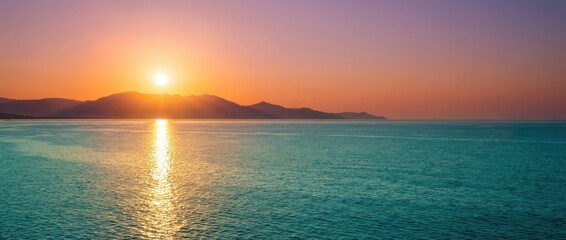 Majestic ocean sunset with vibrant orange sun and purple sky over distant mountains water