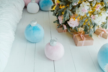 Soft plush Christmas ornaments in pastel blue and pink lie on white wooden floor near decorated tree and wrapped gifts