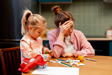 Stressed mother holding head, feeling overwhelmed during child's playtime at home