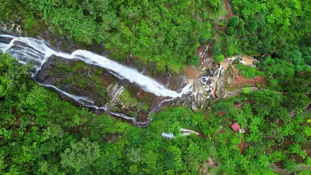 Aerial drone footage of a tall thin waterfall in the green small valley in Dieng plateau, Indonesia, called Swiss van Java, with forests around