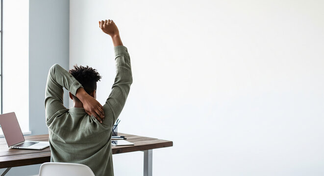 Rear view of young man stretching at minimalist home office desk with copy space