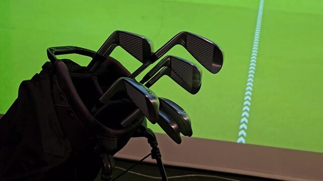 Golf clubs set up in indoor area with simulation background for practice session on a green course