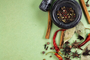 Spices and herbs arranged on green background with mortar and pestle