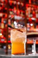 Craft cocktail with smoky aroma at bar. A vibrant cocktail is served with a smoky garnish in a lively bar filled with colorful lights and bottles.