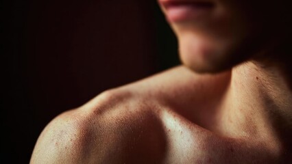 Naklejka premium Close-up of a bare shoulder and neck in warm low light, with part of the chin and lips visible at the top. Concept Close-up Portrait, Warm Low Light, Shoulder and Neck Focus, Soft Lipline