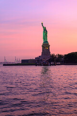 Statue of Liberty at sunset with pink sky. The Statue of Liberty stands against a vivid pink and orange sky at sunset.