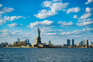 Fototapeta premium Statue of Liberty with Manhattan skyline in the distance. The Statue of Liberty stands tall with the Manhattan skyline visible in the background across the water.