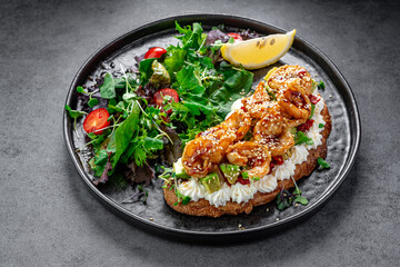 Bruschetta with shrimp and avocado on black plate. Bruschetta with shrimp, avocado, sesame, cream...