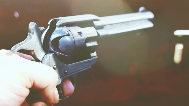 A vintage replica revolver handgun with the hammer cocked. Handheld shot edited with natural lighting, film effects and light leaks.