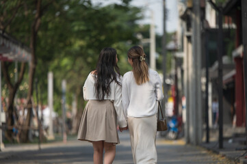 Naklejka premium Two young female friends walking hand in hand down a city street together.