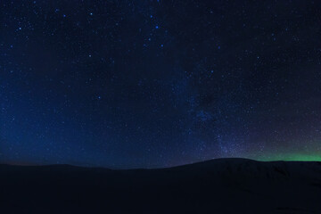 Starry night sky with Aurora over dark mountain