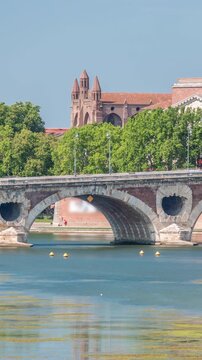 Garonne River and Pont Neuf timelapse with Basilica of Our Lady of the Daurade in downtown Toulouse, France. Renaissance arch bridge reflects in the water under a blue sky. Waterfront with green trees