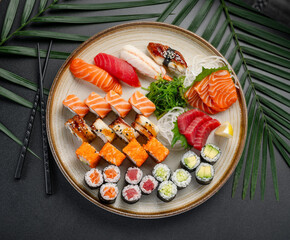Sushi and Sashimi Platter with Rolls and Vegetables. A round platter displays an array of sushi, sashimi, and maki rolls, including tuna, salmon, and eel, with seaweed and vegetables. © white78