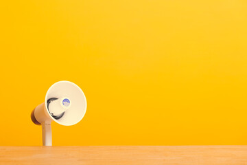 White Megaphone behind wooden table on yellow background - announcement concept