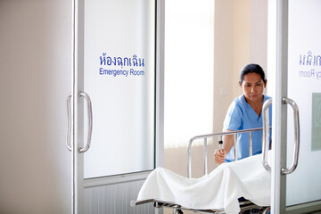 medical staff moving a patient on a stretcher into the emergency room. A male doctor in green scrubs and a female nurse in blue scrubs are carefully guiding the stretcher through the doorway. The sign