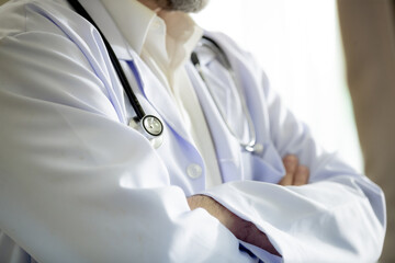 The image shows a medical professional wearing a white lab coat with a stethoscope draped around the neck. The person stands with arms crossed,