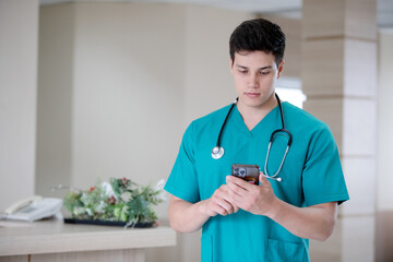 Male doctor wearing lab coat holding cellphone beside windows in hospital