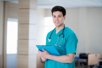 A confident young doctor in green scrubs stands with folded arms, wearing a stethoscope, smiling slightly, representing professionalism and trust in modern healthcare.