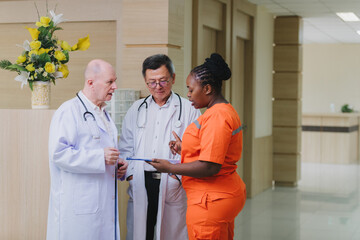 A group of healthcare professionals stands in a hospital corridor, discussing medical documents. Two doctors in white coats and a nurse in bright orange scrubs are engaged in a serious conversation ab