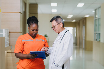 A group of healthcare professionals stands in a hospital corridor, discussing medical documents. Two doctors in white coats and a nurse in bright orange scrubs are engaged in a serious conversation ab