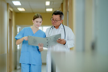 doctor and a nurse standing together in a hospital corridor, reviewing medical documents on a clipboard.