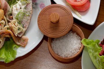 Salt sitting in a wooden bowl beside a fresh meal on a wooden table