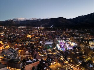 Zakopane - Polska - stolica Polskich Tatr nagrana wieczorem z drona. Swiatła miasta i góry w tle zimową porą podczas zachodu słońca © Konrad