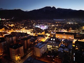 Zakopane - Polska - stolica Polskich Tatr nagrana wieczorem z drona. Swiatła miasta i góry w tle zimową porą podczas zachodu słońca © Konrad
