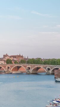 Garonne River and Pont Neuf timelapse with Museum of the History of Medicine in downtown Toulouse, France. This Renaissance arch bridge reflects in water under a blue sky. Waterfront with green trees